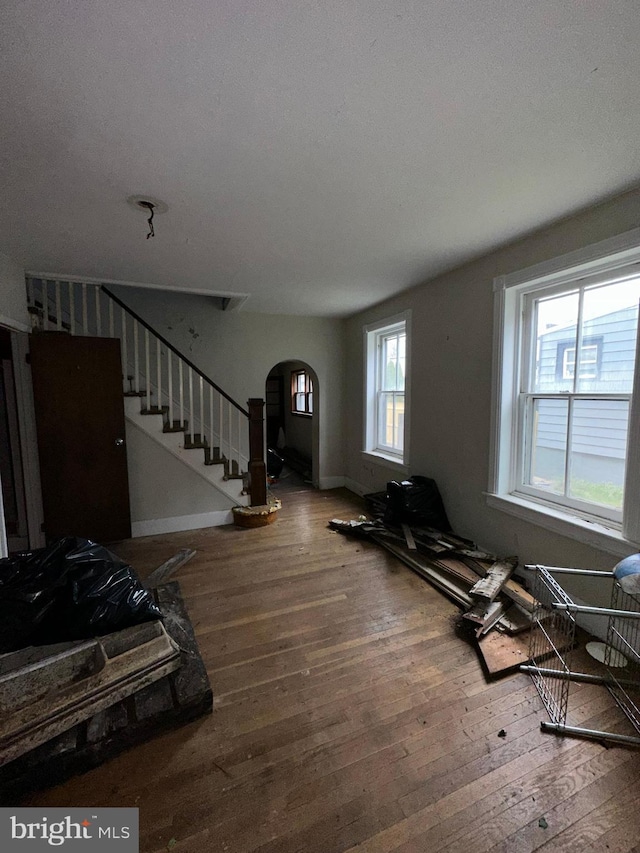 unfurnished living room with baseboards, arched walkways, stairway, and wood-type flooring