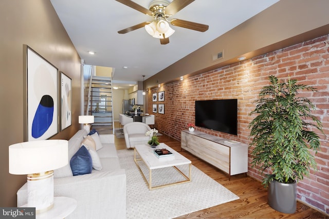 living room with ceiling fan, brick wall, and hardwood / wood-style floors