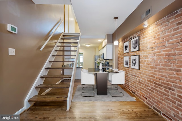 staircase with brick wall and wood-type flooring