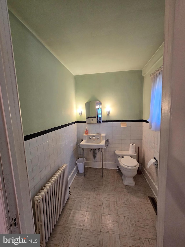 bathroom featuring radiator, sink, tile walls, and toilet