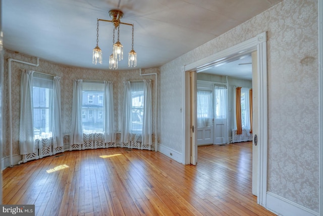 unfurnished dining area with light wood-type flooring, an inviting chandelier, and plenty of natural light