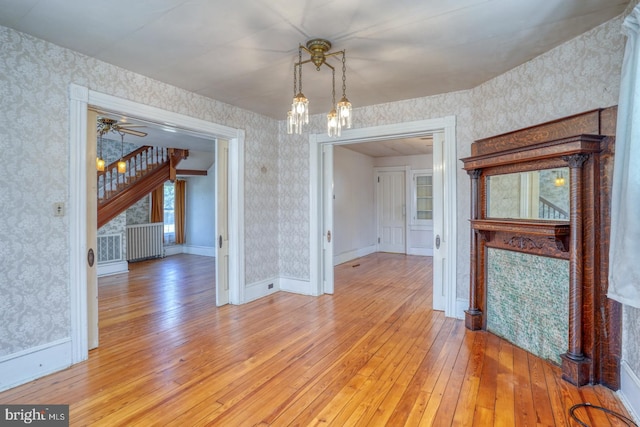 unfurnished dining area featuring ceiling fan with notable chandelier, light hardwood / wood-style floors, and radiator