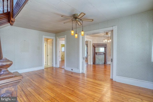 unfurnished living room featuring ceiling fan with notable chandelier and light wood-type flooring