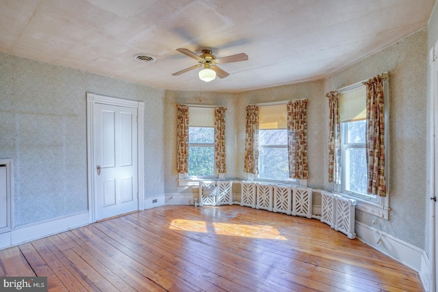 unfurnished room with radiator, light wood-type flooring, and ceiling fan