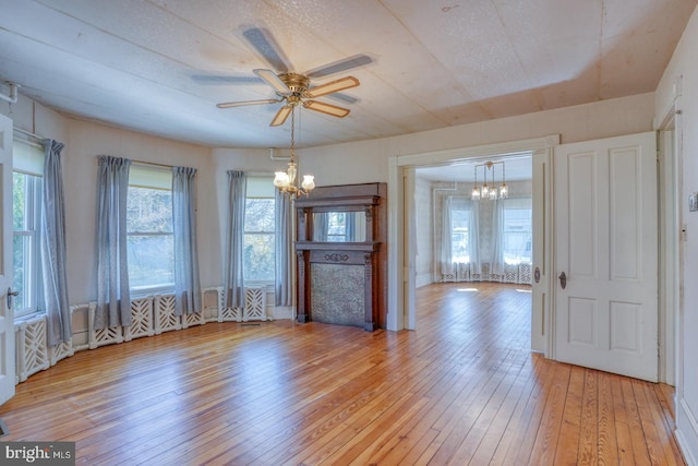 unfurnished living room featuring ceiling fan with notable chandelier and light hardwood / wood-style flooring