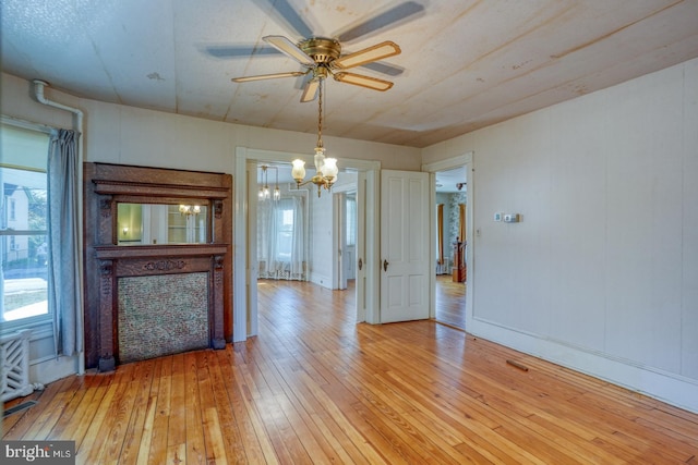 unfurnished living room with ceiling fan with notable chandelier and light wood-type flooring