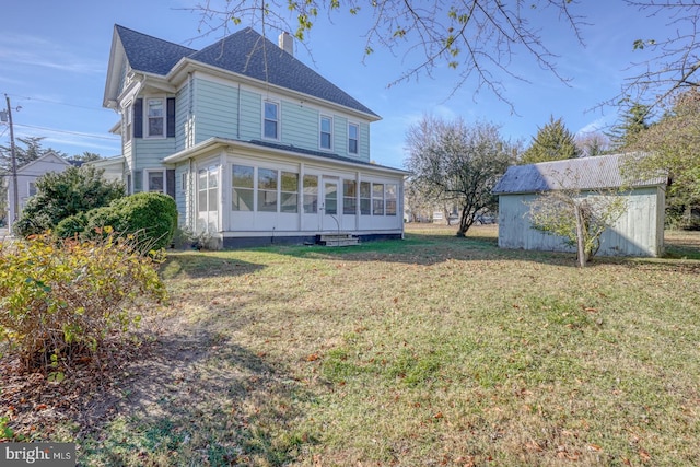 rear view of property featuring a sunroom, a yard, and a shed