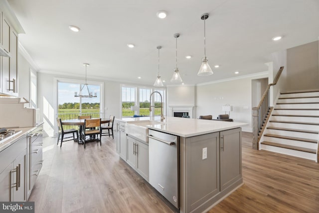 kitchen with decorative light fixtures, stainless steel dishwasher, crown molding, light hardwood / wood-style flooring, and a center island with sink