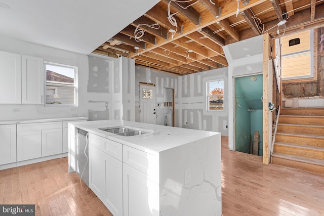 kitchen featuring white cabinetry, light wood-style flooring, a sink, dishwasher, and a kitchen island with sink
