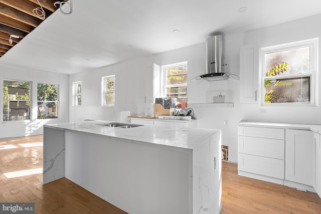 kitchen featuring light wood finished floors, light stone countertops, wall chimney range hood, and a healthy amount of sunlight