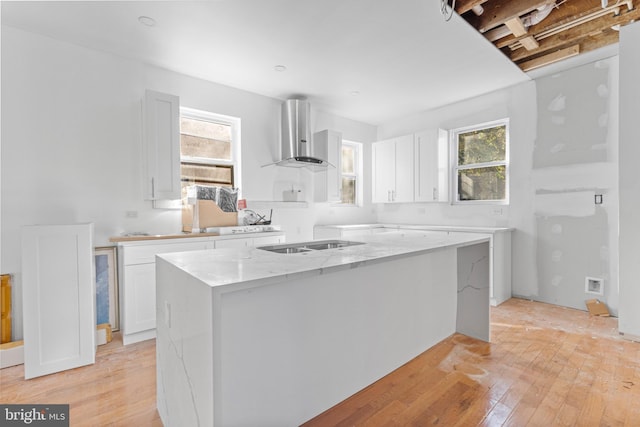 kitchen with light stone counters, light wood-style flooring, wall chimney range hood, and white cabinetry