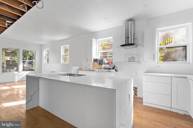 kitchen featuring a kitchen island, extractor fan, white cabinetry, light stone countertops, and light hardwood / wood-style floors