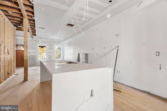 kitchen featuring light hardwood / wood-style flooring, light stone countertops, and a center island with sink