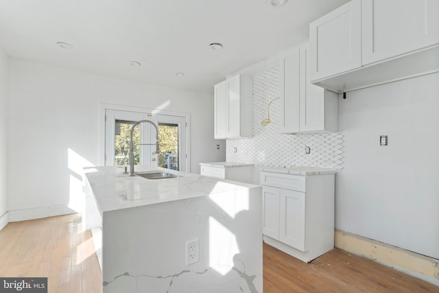 kitchen featuring sink, light wood-type flooring, an island with sink, white cabinets, and light stone counters