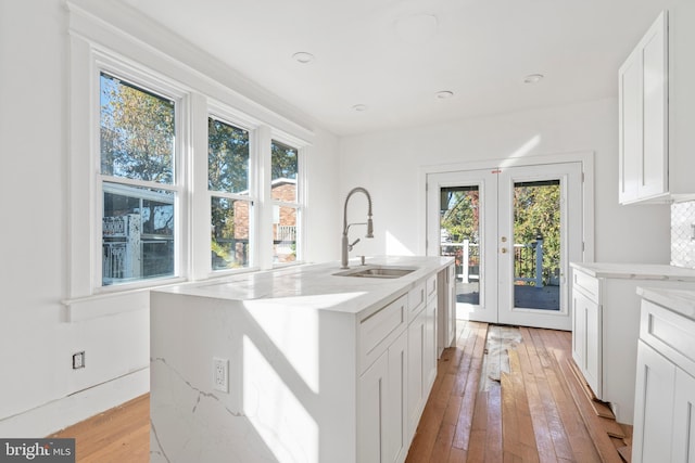 kitchen with an island with sink, light hardwood / wood-style flooring, sink, white cabinets, and light stone counters