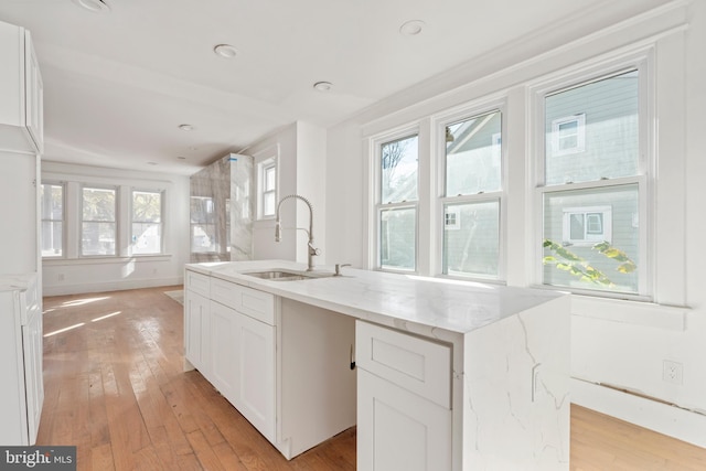 kitchen featuring white cabinetry, a kitchen island with sink, sink, and light wood-type flooring