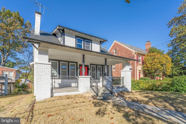 bungalow with a front yard, a chimney, a porch, and brick siding