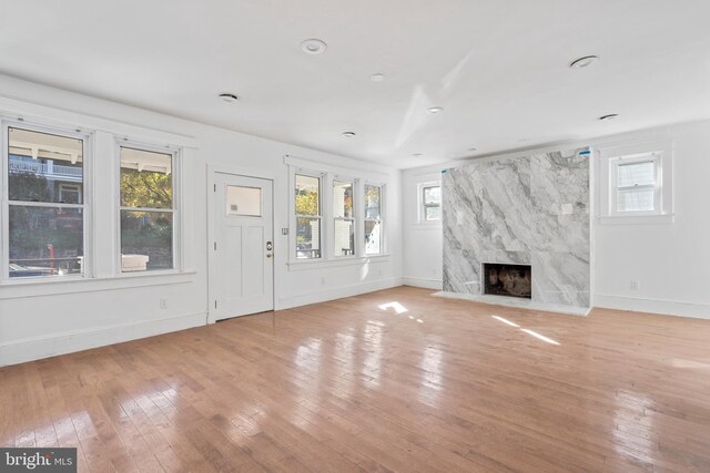 unfurnished living room with a wealth of natural light, light wood-style floors, and a high end fireplace