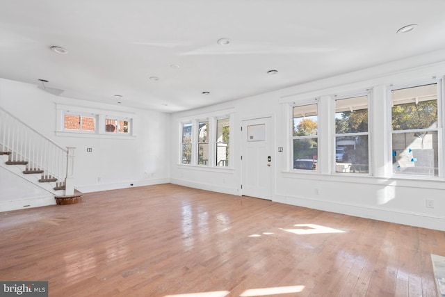 unfurnished living room featuring baseboards, stairway, and light wood-style floors