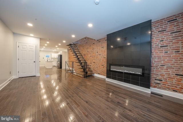 unfurnished living room featuring dark hardwood / wood-style floors, brick wall, and a fireplace