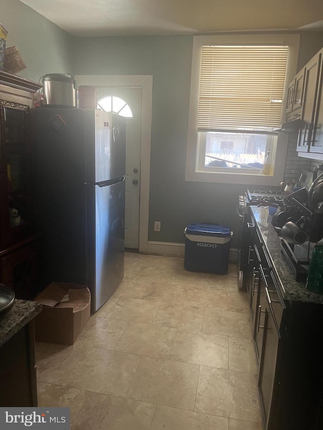 kitchen with stainless steel fridge, decorative backsplash, and dark stone counters