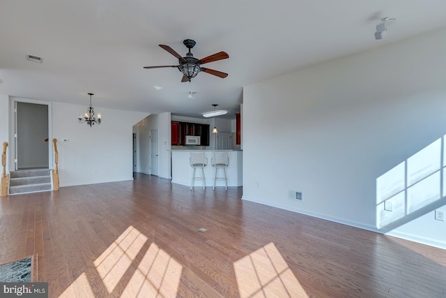 unfurnished living room with ceiling fan with notable chandelier and dark wood-type flooring