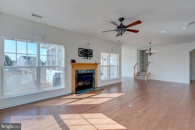 unfurnished living room with ceiling fan with notable chandelier, hardwood / wood-style floors, and a fireplace