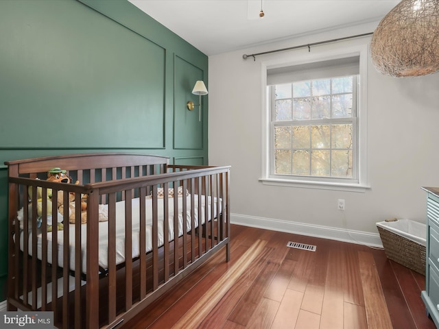 bedroom featuring a nursery area and dark wood-type flooring