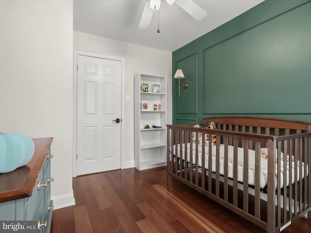 bedroom with a nursery area, dark hardwood / wood-style floors, and ceiling fan