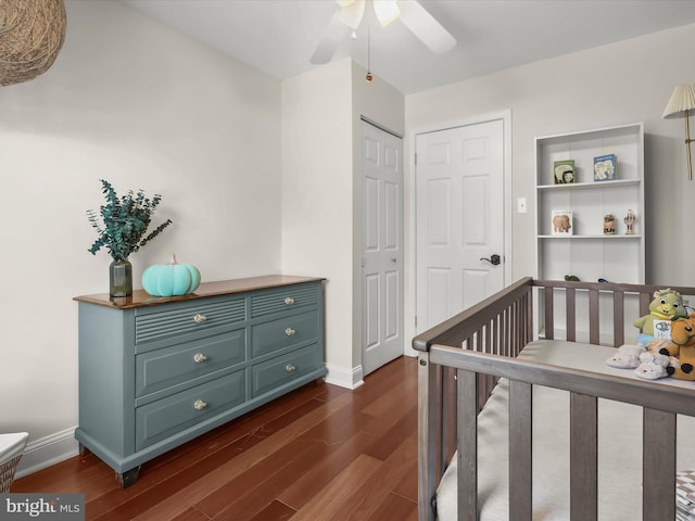 bedroom featuring a nursery area, ceiling fan, dark wood-type flooring, and a closet