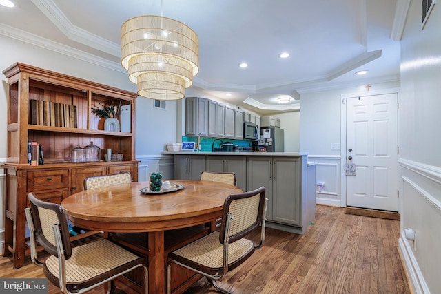 dining area featuring light wood-type flooring, a chandelier, sink, and crown molding