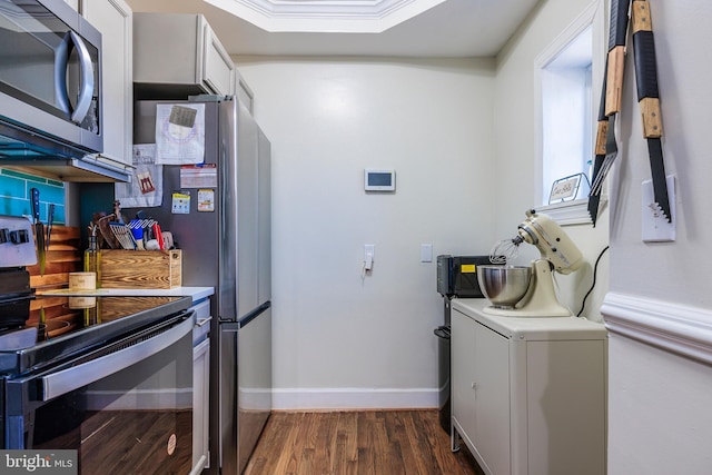 kitchen with appliances with stainless steel finishes, a tray ceiling, washer / dryer, crown molding, and dark hardwood / wood-style flooring