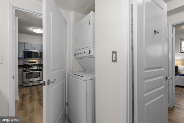 laundry area with a textured ceiling, dark hardwood / wood-style flooring, and stacked washer and clothes dryer