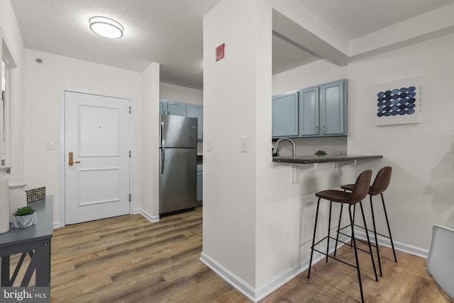 kitchen featuring a kitchen bar, a textured ceiling, kitchen peninsula, stainless steel fridge, and dark wood-type flooring