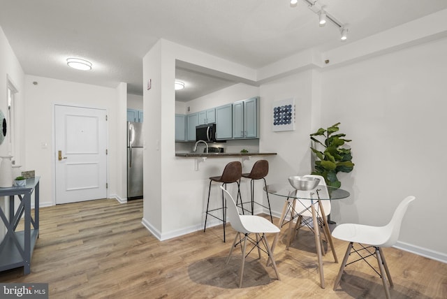 kitchen with kitchen peninsula, appliances with stainless steel finishes, a kitchen breakfast bar, light wood-type flooring, and blue cabinets