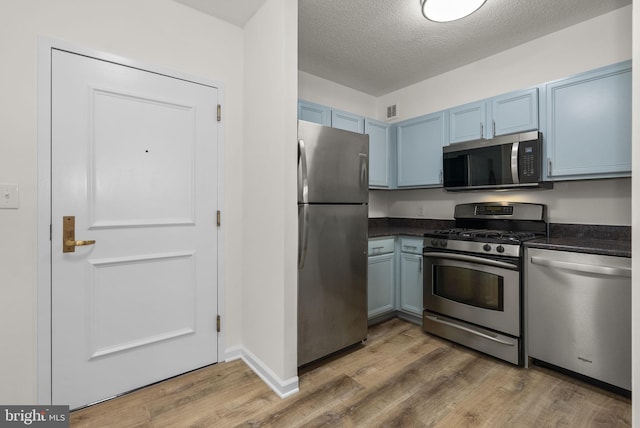 kitchen with blue cabinetry, stainless steel appliances, a textured ceiling, and hardwood / wood-style floors