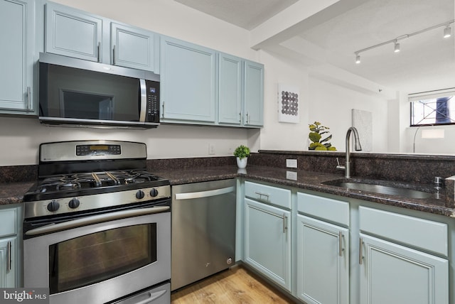 kitchen with sink, appliances with stainless steel finishes, light hardwood / wood-style floors, and dark stone counters