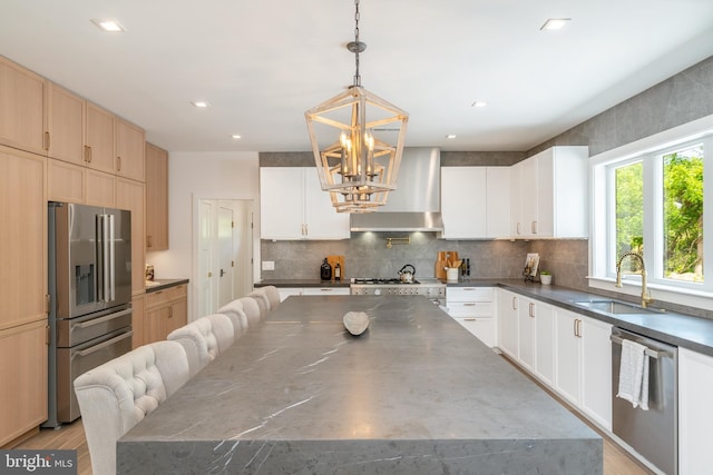 kitchen with wall chimney range hood, sink, a spacious island, stainless steel appliances, and decorative light fixtures