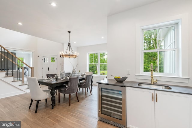 dining space with light hardwood / wood-style flooring, sink, an inviting chandelier, and beverage cooler