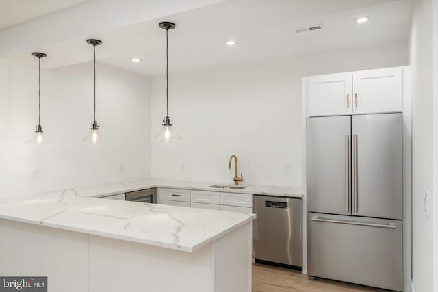 kitchen featuring appliances with stainless steel finishes, kitchen peninsula, decorative light fixtures, and white cabinetry