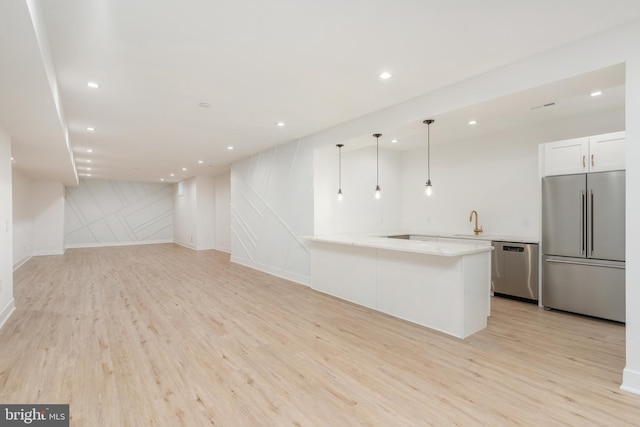 kitchen with appliances with stainless steel finishes, hanging light fixtures, white cabinets, light stone counters, and light hardwood / wood-style flooring