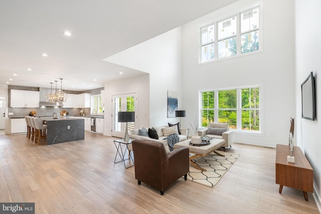 living room with light hardwood / wood-style floors, a notable chandelier, and a towering ceiling