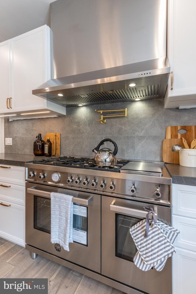 kitchen with white cabinetry, wall chimney exhaust hood, light wood-type flooring, and double oven range