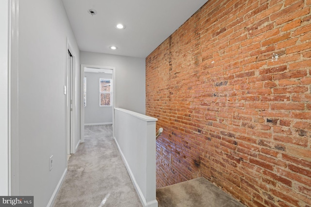 hall featuring light colored carpet and brick wall