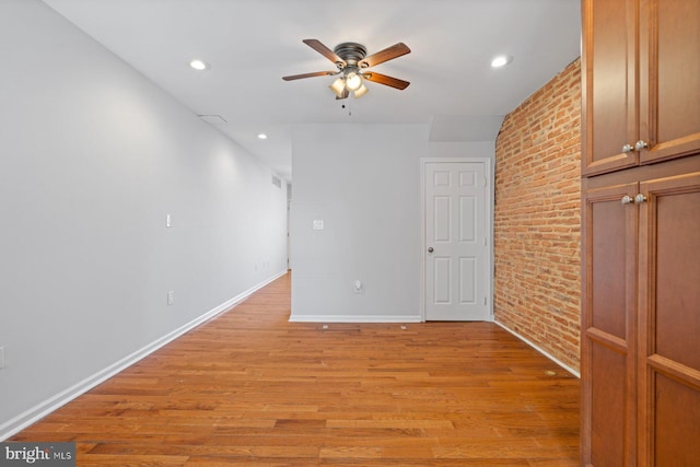 unfurnished room featuring light hardwood / wood-style flooring, ceiling fan, and brick wall