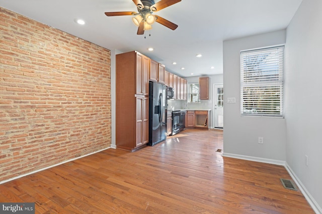 kitchen with black appliances, ceiling fan, hardwood / wood-style floors, and brick wall