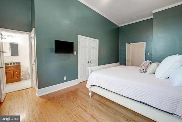 bedroom featuring baseboards, ornamental molding, a sink, light wood-type flooring, and a closet