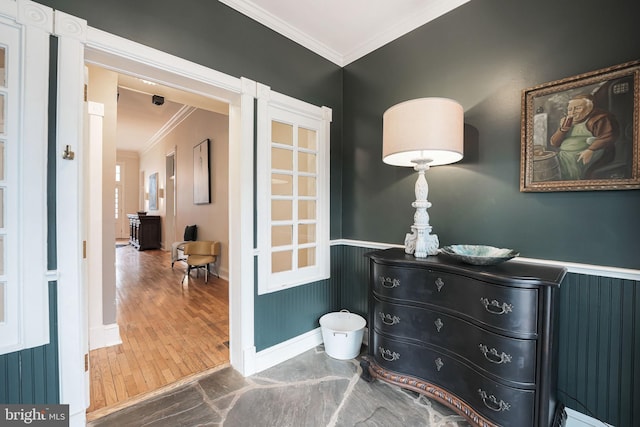 interior space with ornamental molding, a wainscoted wall, baseboards, and wood finished floors