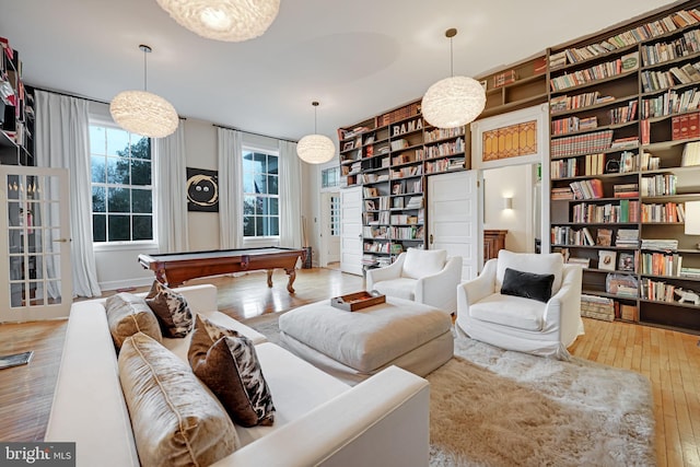 living area with light wood-style floors, pool table, and wall of books