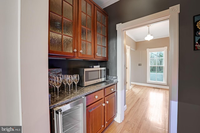 kitchen with brown cabinetry, dark stone counters, wine cooler, stainless steel microwave, and light wood-style floors